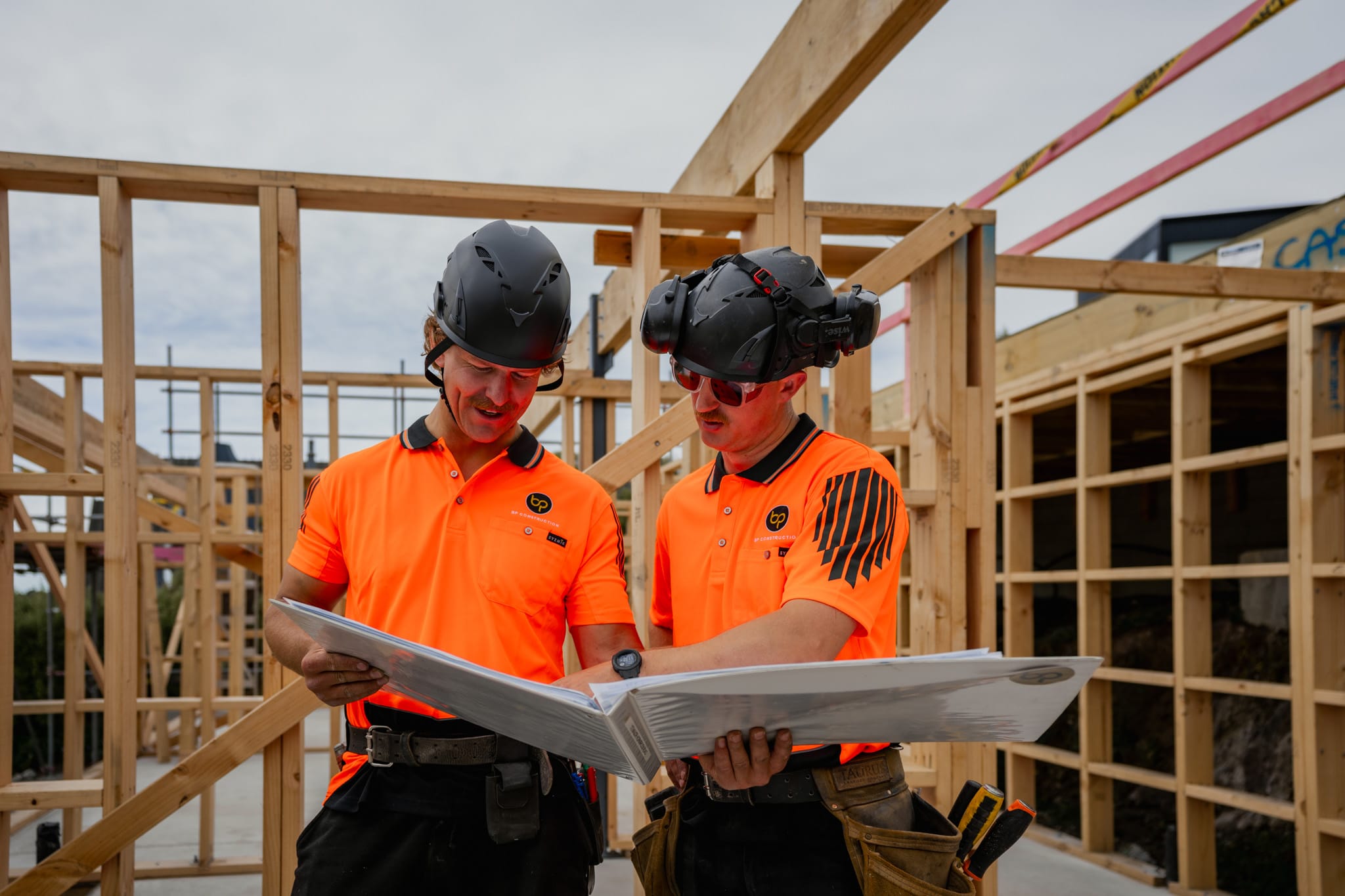 Builders reviewing construction plans on a timber framed site, highlighting teamwork, planning accuracy, and professional construction management.