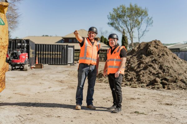 Two site managers in high-vis gear discussing progress on a housing development, representing construction NZ capability, building construction oversight and the coordinated manage construction projects approach used across new home developments and Aged care refurbishment work.