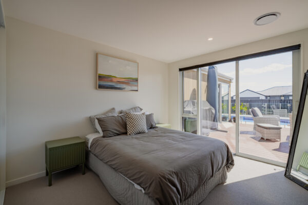 Modern bedroom in a newly built home with soft neutral styling, opening to a sunny deck and pool area, showcasing quality residential construction and architectural home design.
