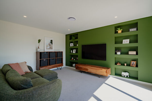 Stylish living room in a newly built house, featuring a green feature wall with built-in shelving, modern furnishings, and architectural interior design reflecting high-quality home construction standards.