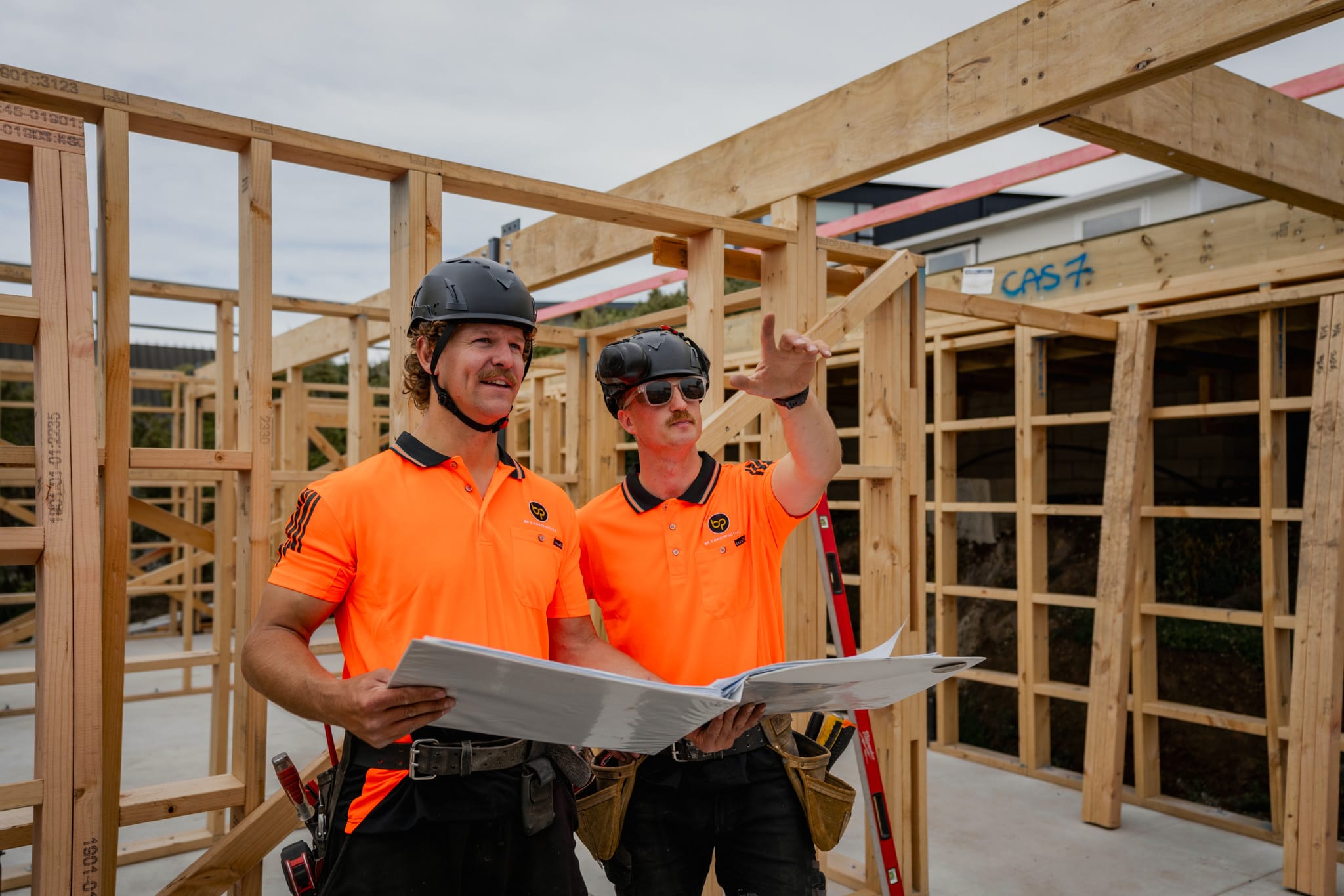 Two builders assessing framing for a new build home, guiding construction projects through planning, building construction checks, building inspection report needs, and ensuring the architectural plans suit an architecturally designed home.