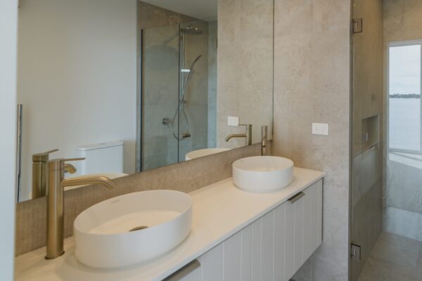 A contemporary bathroom with dual basins, tiled finishes and premium fixtures inside an architecturally designed home, representing bespoke refurbishment, home construction, renovations and commercial fit out standards applied in new build houses.