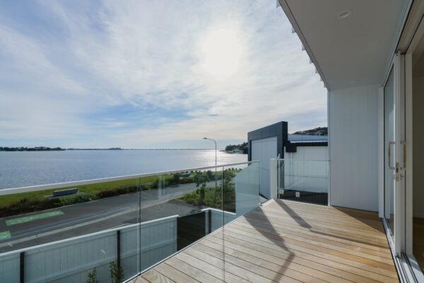 A balcony of a modern house overlooking the water, showcasing a bespoke architectural build within new build homes and new housing developments. Highlights Design and build quality, home construction, property inspection report readiness and construction NZ expertise.