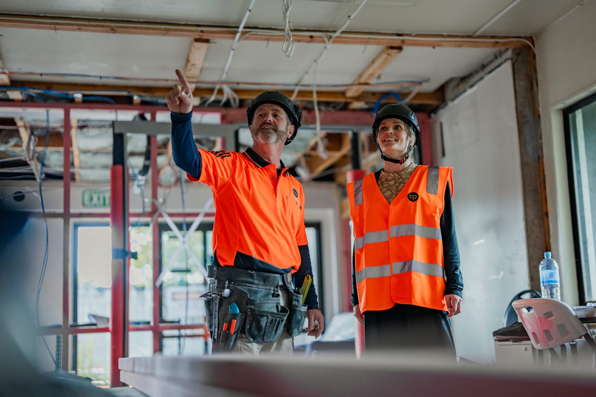 Two workers reviewing architectural plans inside a site undergoing bespoke refurbishment, illustrating construction and management, commercial fit out capability, property inspection report preparation, and Design and build services for architecturally designed homes and new build developments.