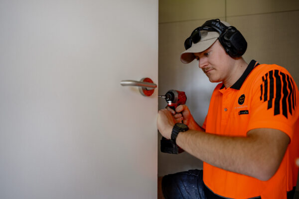 A tradesperson installing door hardware during interior refurbishment, illustrating home construction skill, building construction tasks, Commercial Construction capability and support for building inspection report and property inspection report requirements.
