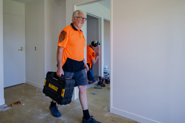 A builder carrying tools through a home undergoing renovations, highlighting bespoke refurbishment, Aged care construction, home repair insurance work, project construction and a homebuilding company’s ability to manage construction projects efficiently.