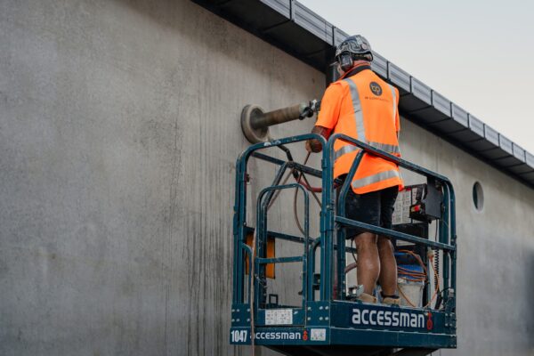 A construction worker operating equipment on an elevated platform while completing exterior Commercial Construction tasks, representing bespoke refurbishment, building construction, construction and management and commercial fit out works.